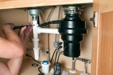 Plumber repairing a garbage disposal beneath a kitchen sink in El Cajon