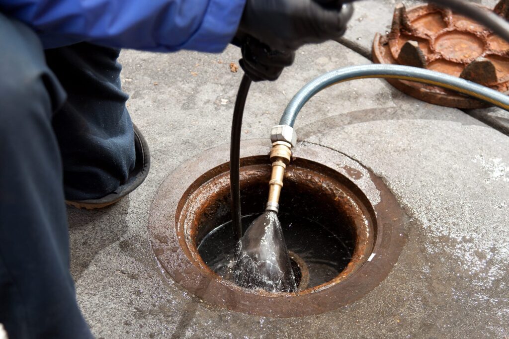 Plumber hydro jetting a sewer line through a manhole in El Cajon